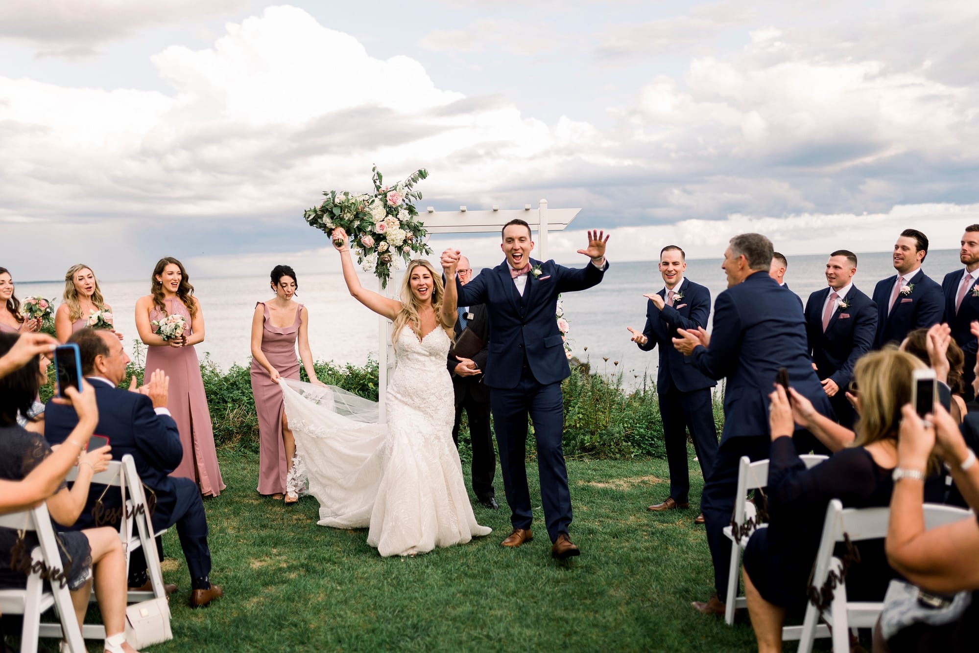 couple coming down the aisle cheering with cape cod ocean in the background Boston cape cod wedding videographer
